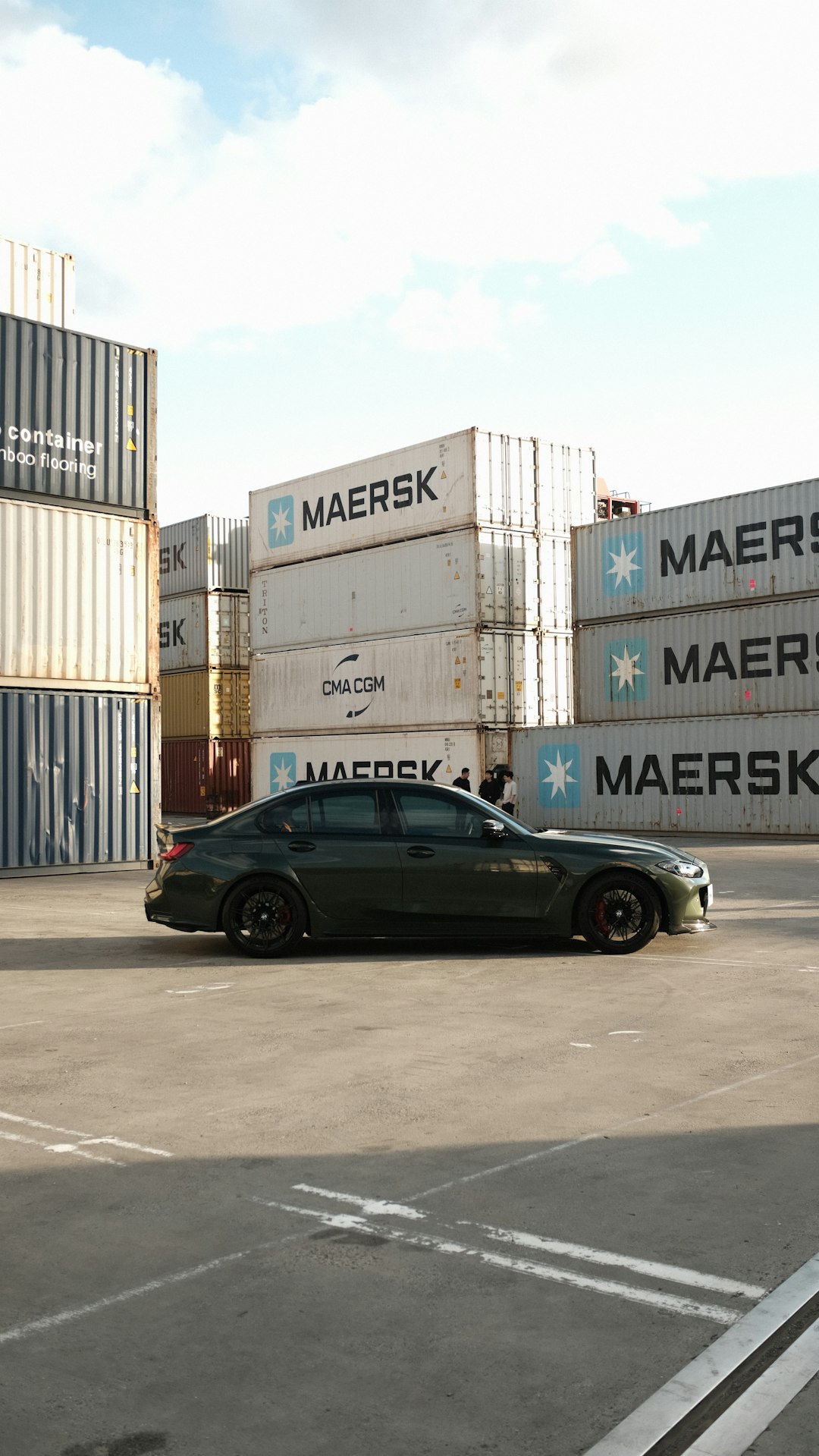 dark-sedan-parked-near-stacked-shipping-containers-87dn-k0qsd4